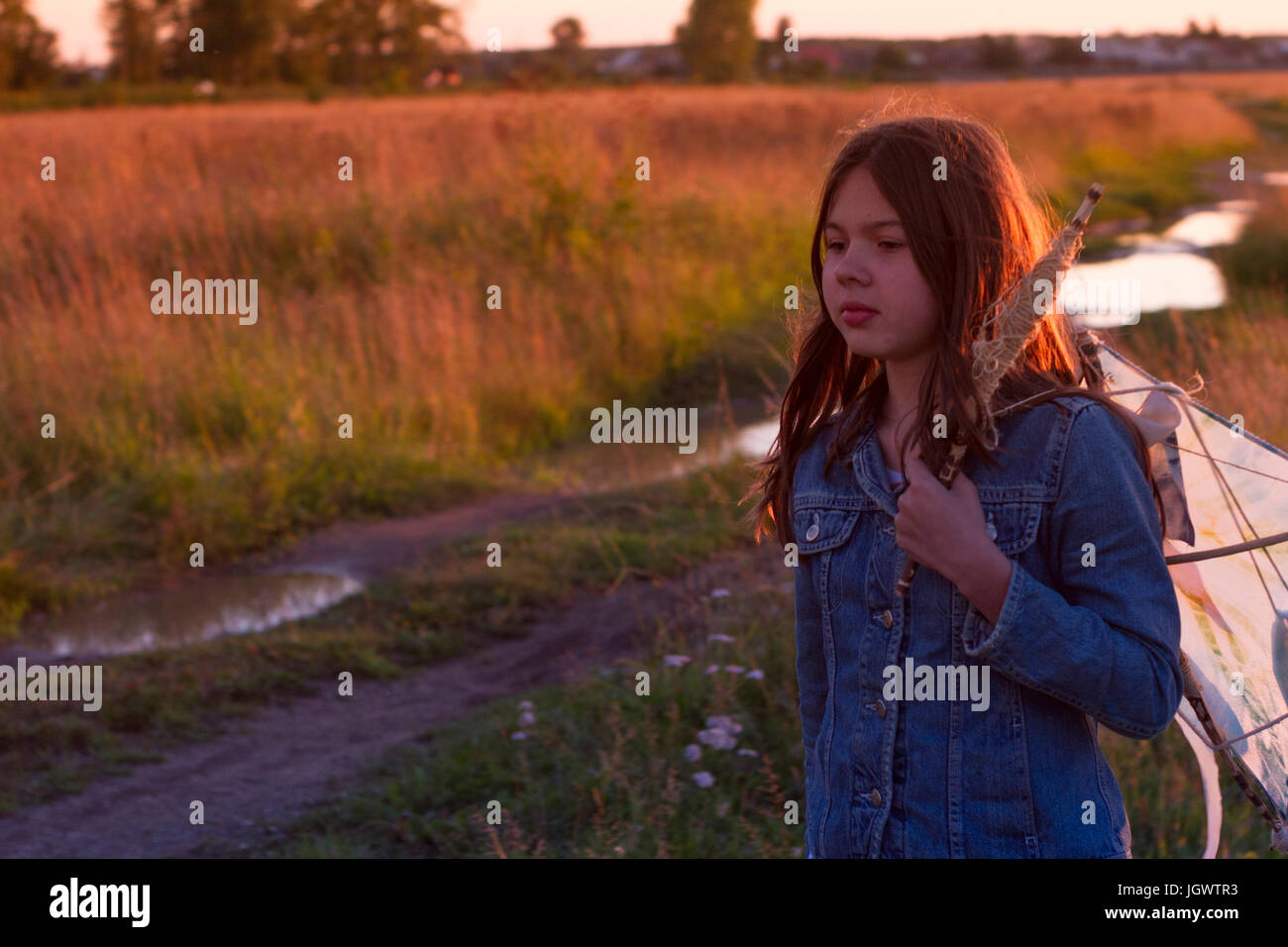 Teenage girl carrying kite over her shoulder along dirt track at sunset Stock Photo