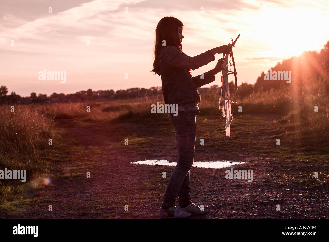 Teenage girl preparing kite on dirt track at sunset Stock Photo