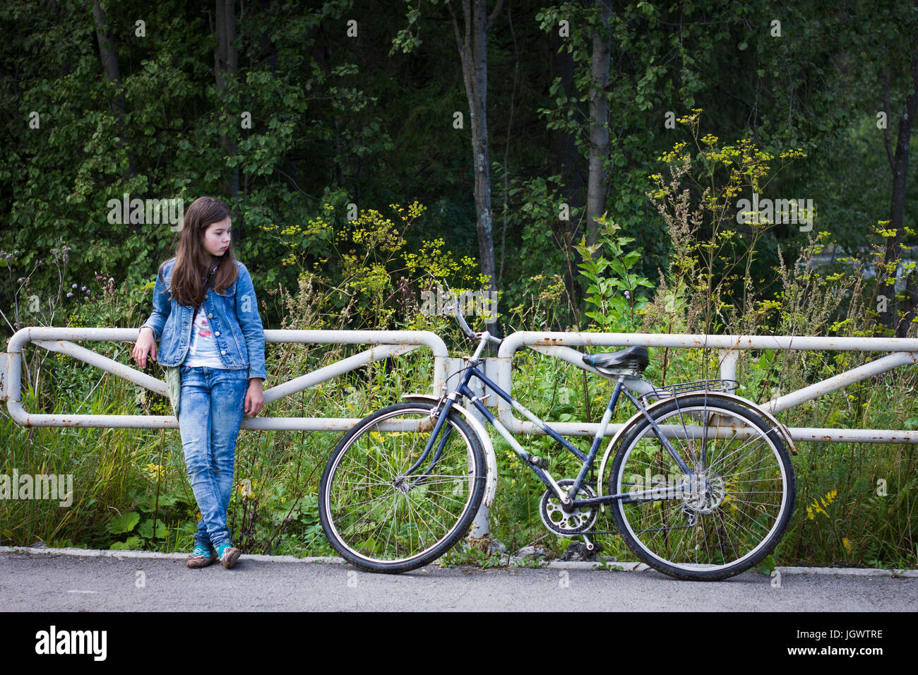 Teenage girl looking at her bicycle on rural road Stock Photo