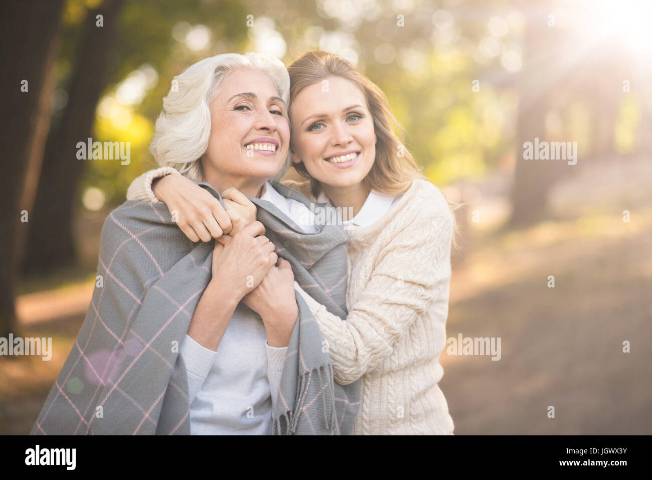 Cherishing family picnic. Mature amused smiling woman enjoying picnic and expressing joy while covering with blanket and hugging aged parent Stock Photo