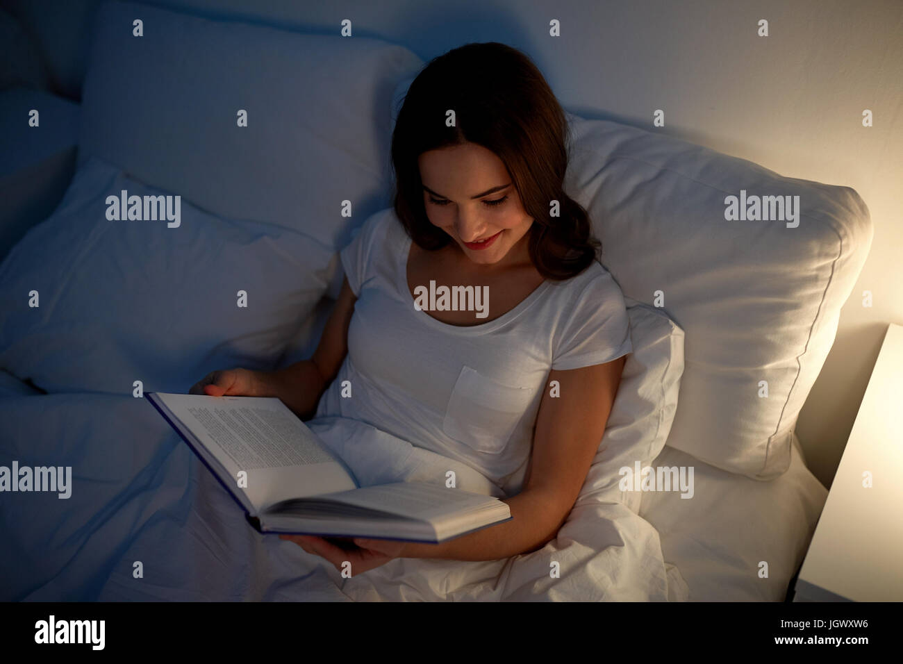 young woman reading book in bed at night home Stock Photo