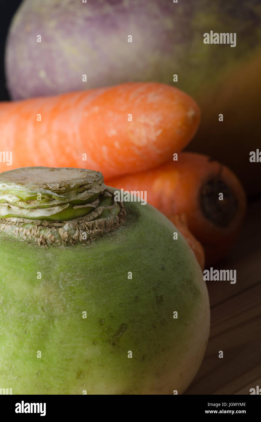 Close up of unwashed; imperfect; raw root vegetables on wooden table, with green turnip in foreground and carrots and swede in soft focus background. Stock Photo
