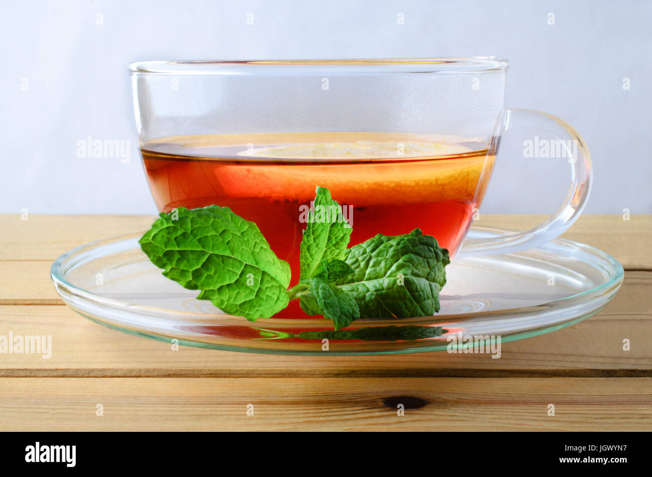Close up of a glass cup of lemon tea with floating lemon slice and a sprig of mint leaves on the saucer.  Resting on a wood planked table and shot at  Stock Photo