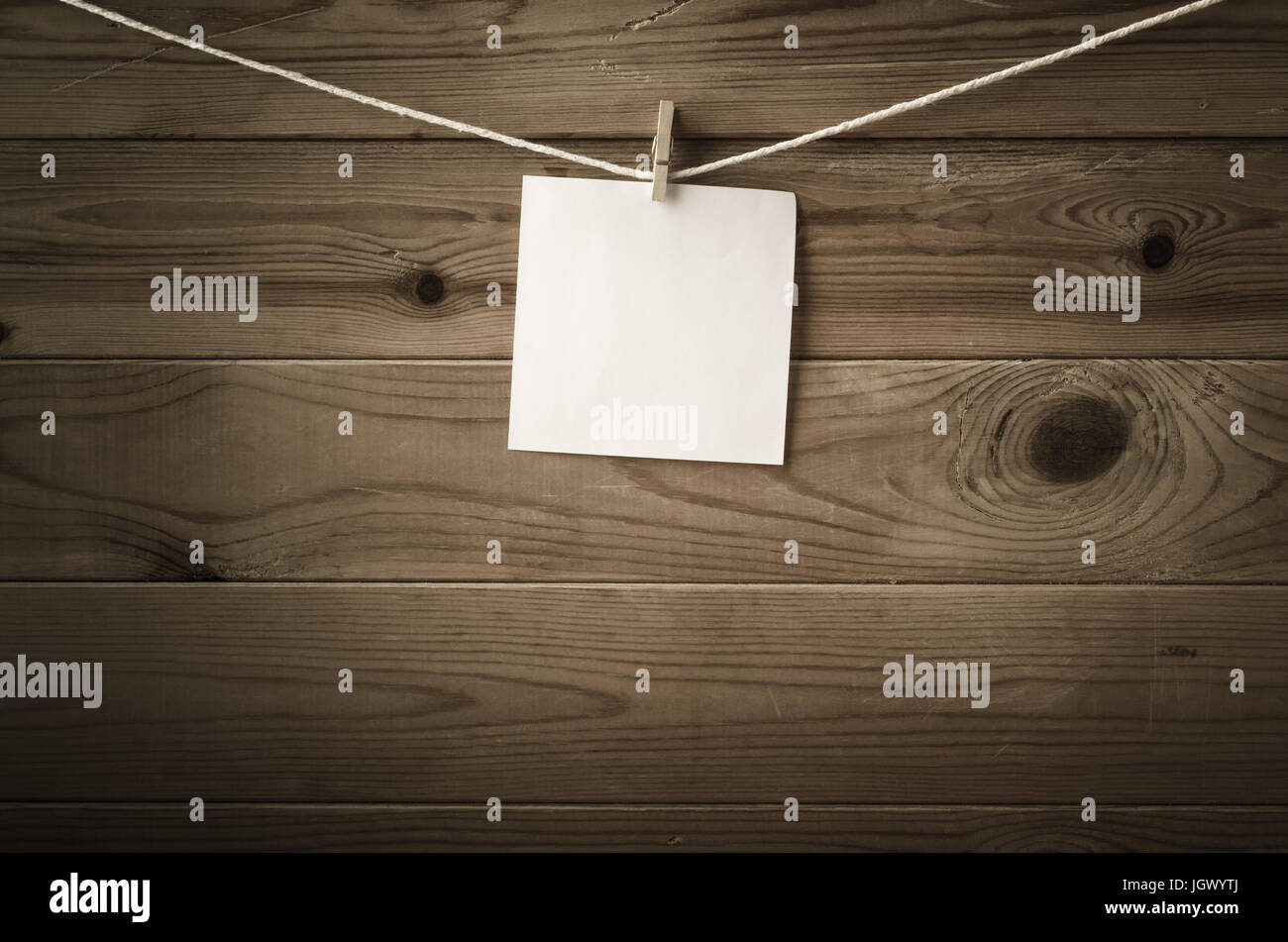 One individual square of note paper, pegged to a string washing line, with wood plank fence in the background.  Low saturation and vignette gives a re Stock Photo