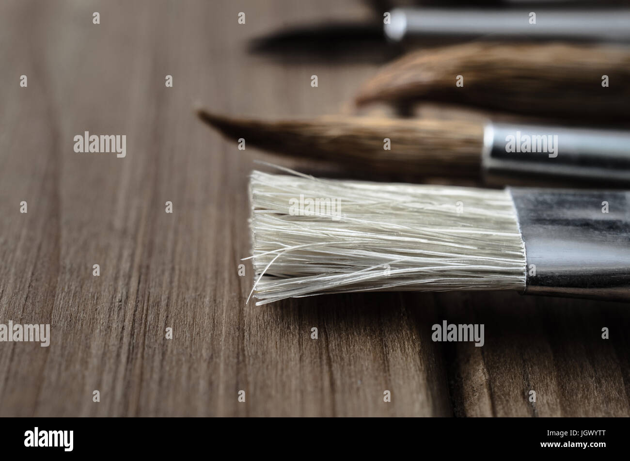 Side view close up of a variety of artist's paintbrushes, laid out in a row on a wood plank table. Stock Photo