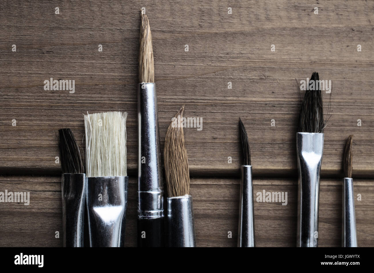Overhead photograph of a variety of artist's paintbrushes arranged on old, faded wood. Stock Photo