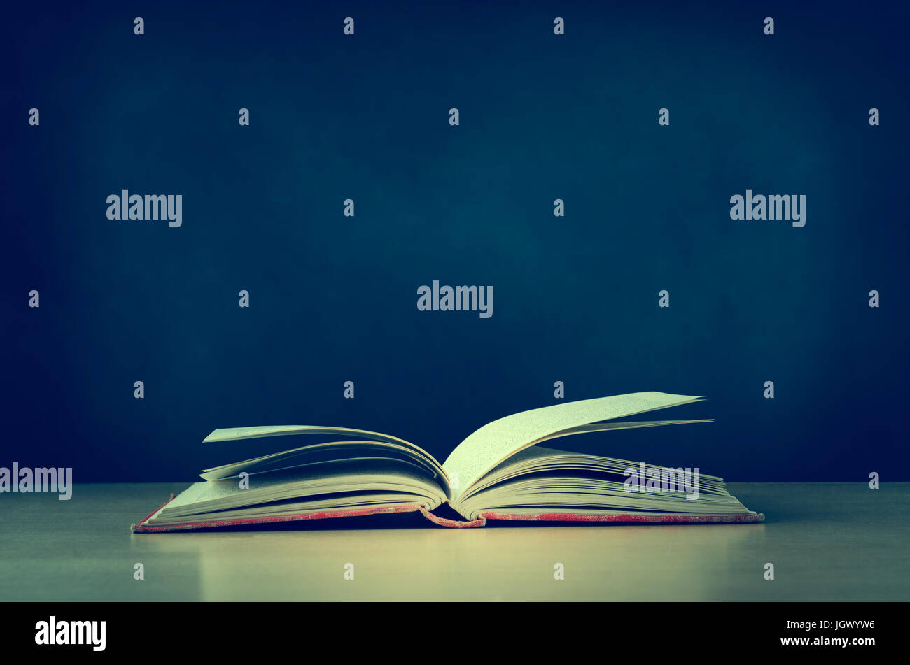 An old, worn, fabric covered red text book, lying opened on a school or college classroom desk.  Blackboard background provides copy space.  Crossproc Stock Photo