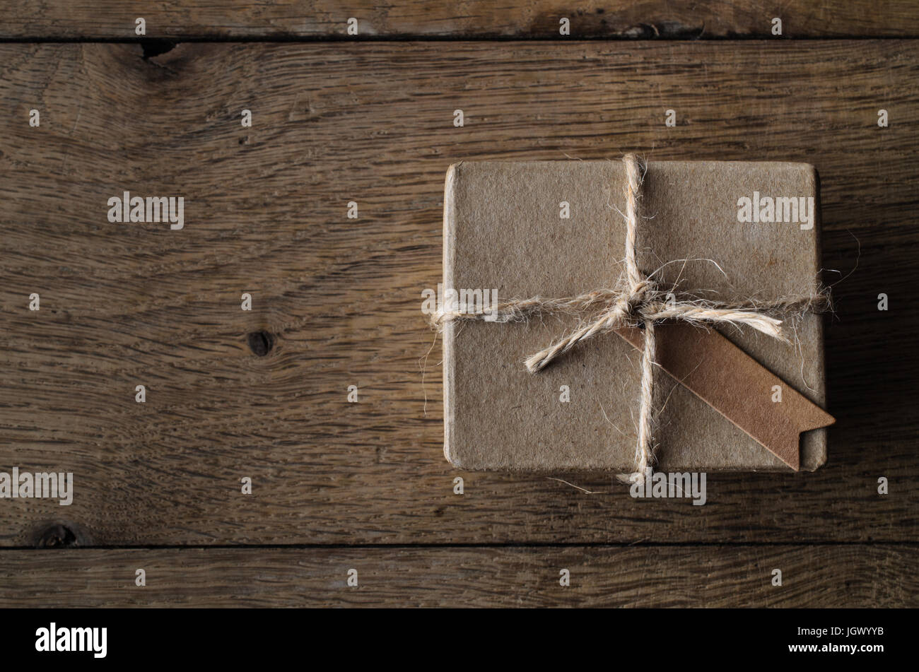 A simple, string tied gift box or package with a blank vintage style label tag.  Shot overhead on an old oak wood planked table. Stock Photo