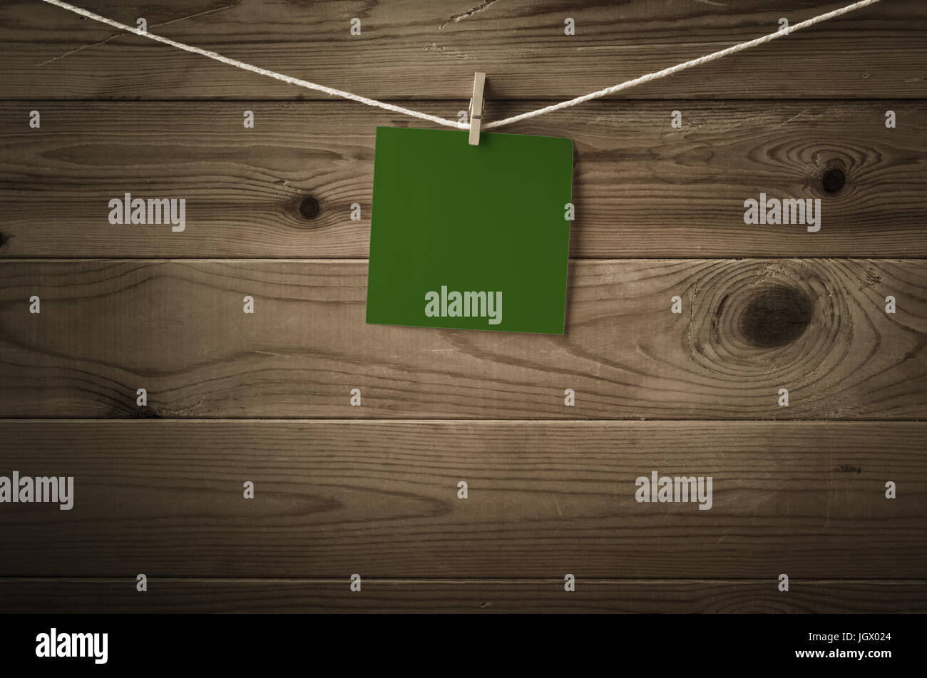 One individual square of festive dark green note paper, pegged to a string washing line with wood plank fence behind.  Low saturation and vignette giv Stock Photo