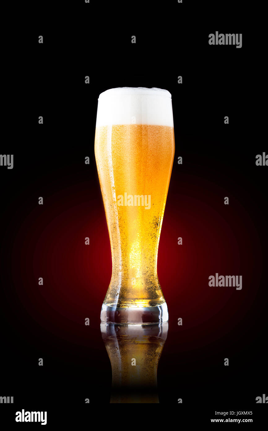 Large glass of cold beer against black and red background. Stock Photo