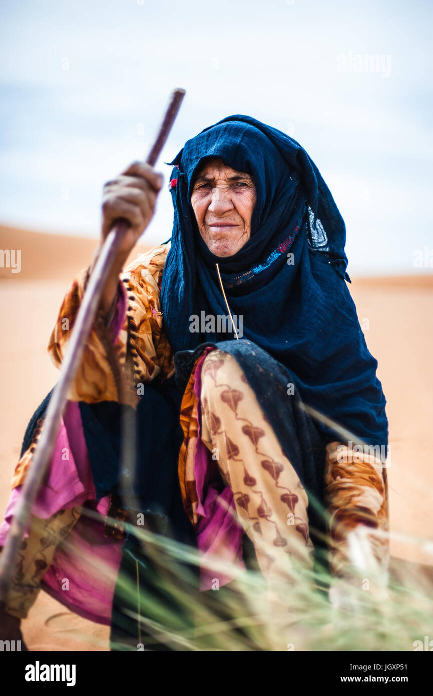 Portrait of old Berber woman sitting on a sand dune in Merzouga, Morocco Stock Photo
