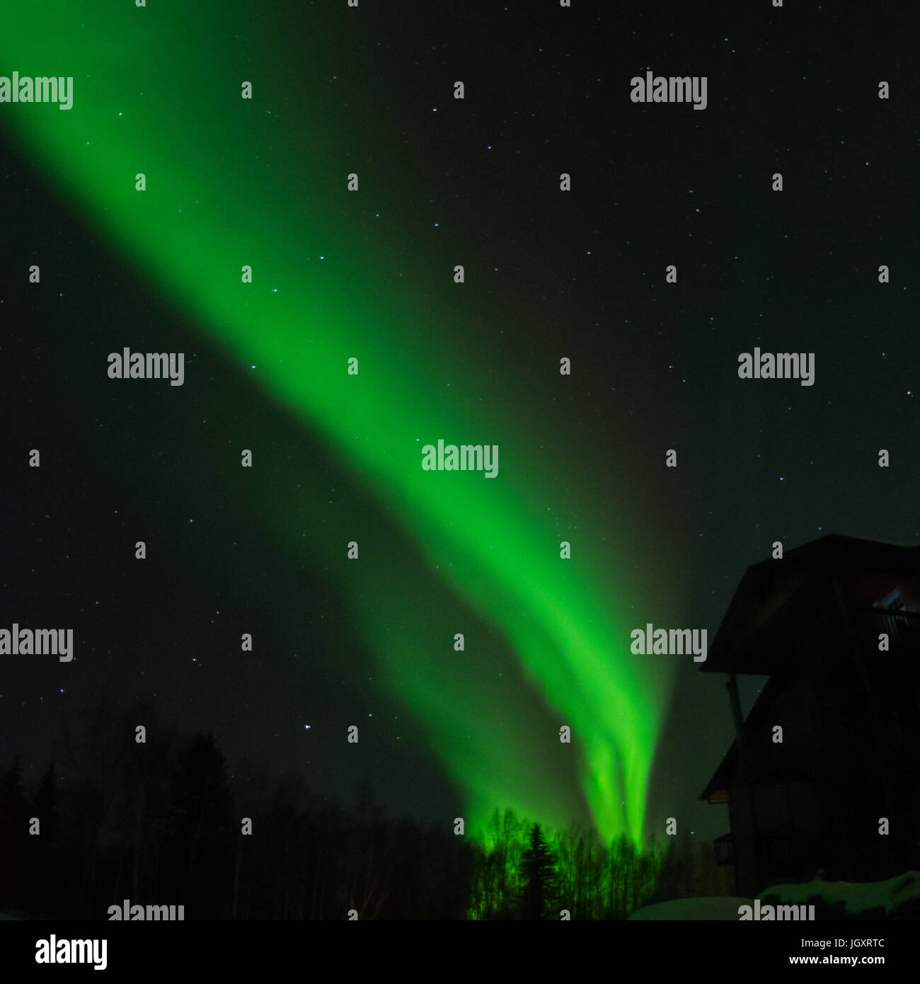 Rising like smoke from the horizon a green aurora reaches away from the house. Stock Photo