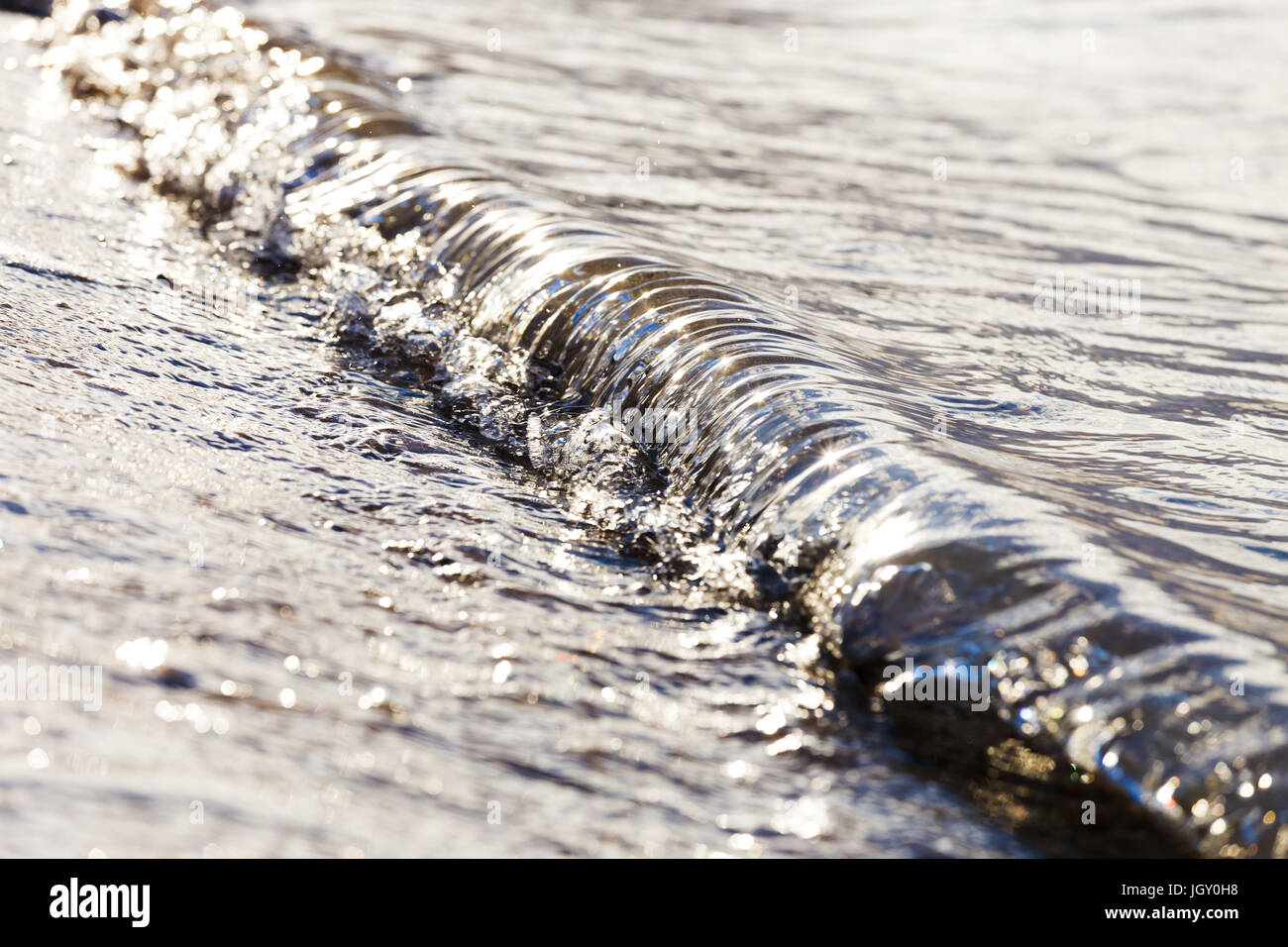 A small wave crashes on the beach in metallic morning light. Stock Photo