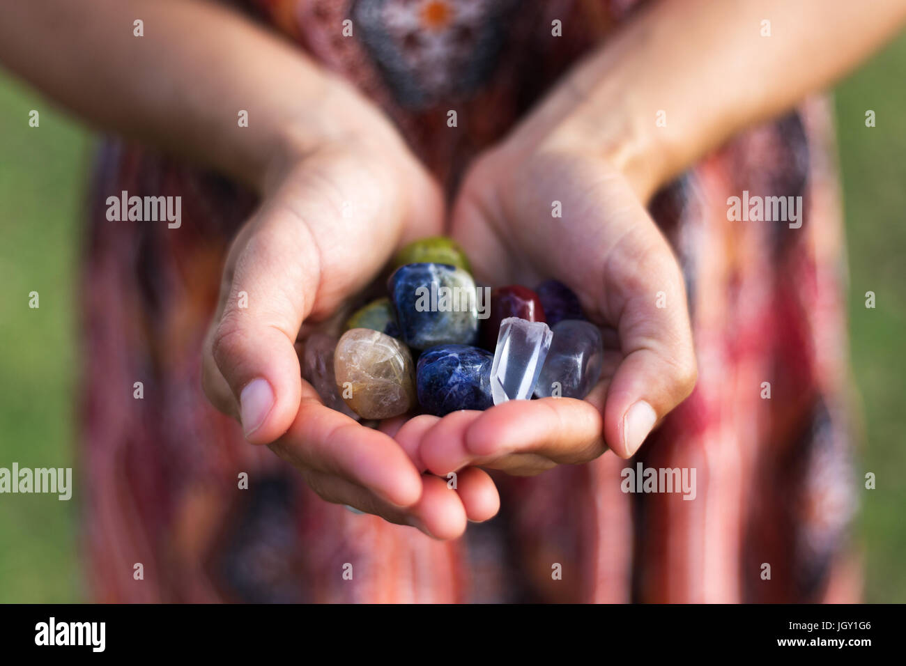 A young woman carefully holds a selection of vibrant gemstones as they reflect the soft sunlight. Stock Photo