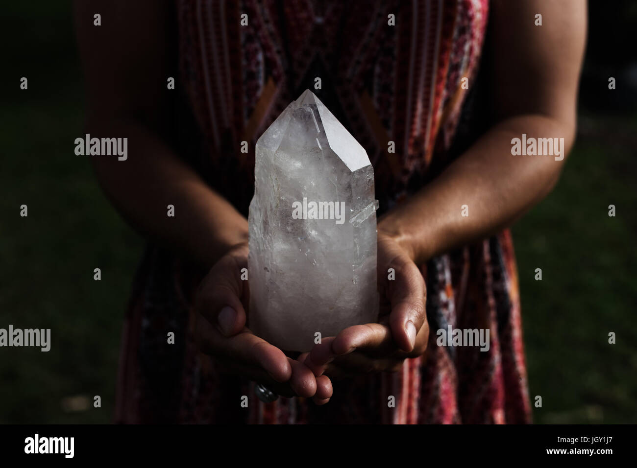 A young woman holding a large, luminous quartz crystal appears powerful in dramatic lighting. Stock Photo