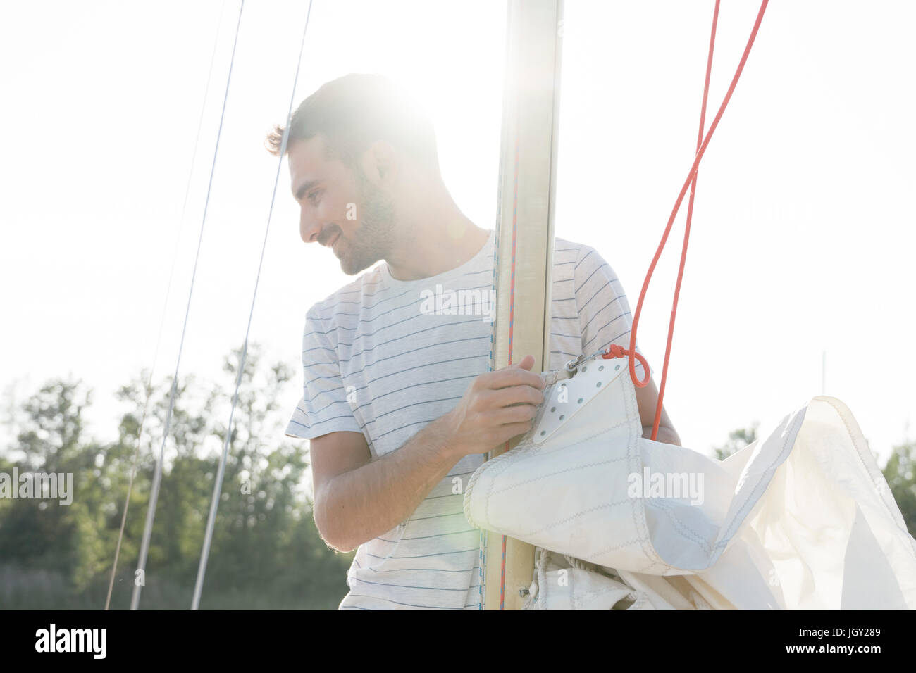 Man on sailing boat, taking down sail Stock Photo