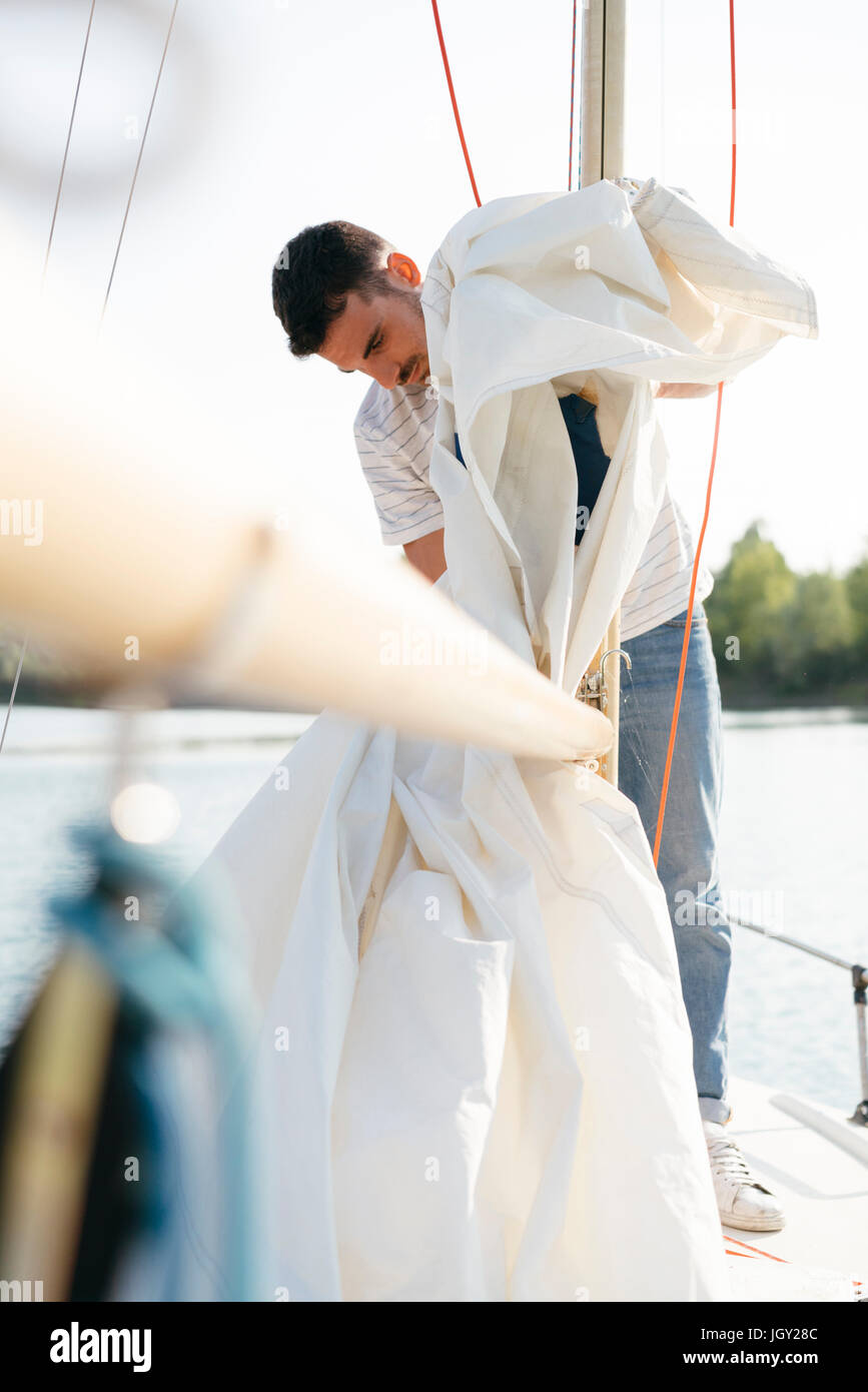Man on sailing boat, taking down sail Stock Photo