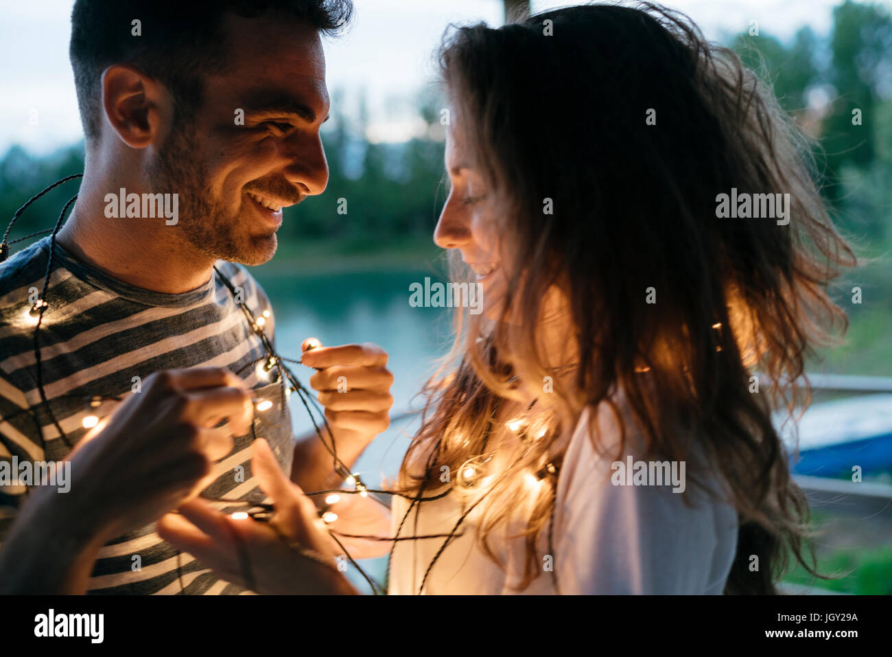 Man and woman standing face to face, illuminated fairy lights wrapped around their neck, smiling Stock Photo