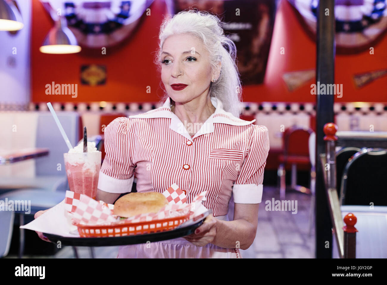 Mature female waitress serving burger in 1950's diner Stock Photo