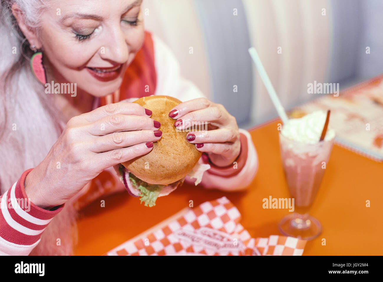 Mature woman eating burger in 1950's diner Stock Photo