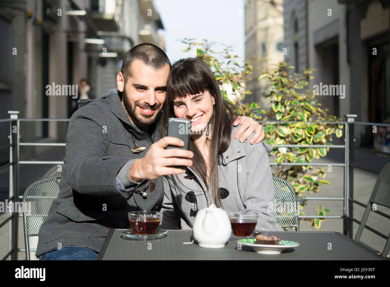 Young couple sitting outside cafe, taking selfie, using smartphone Stock Photo