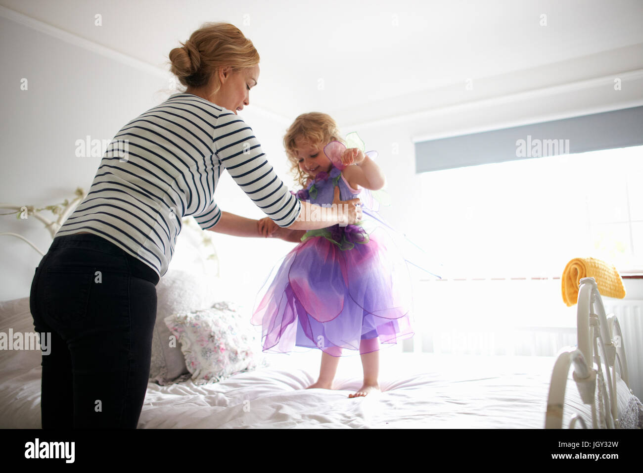 Young girl dressed in fairy costume, standing on bed, mother lifting her Stock Photo