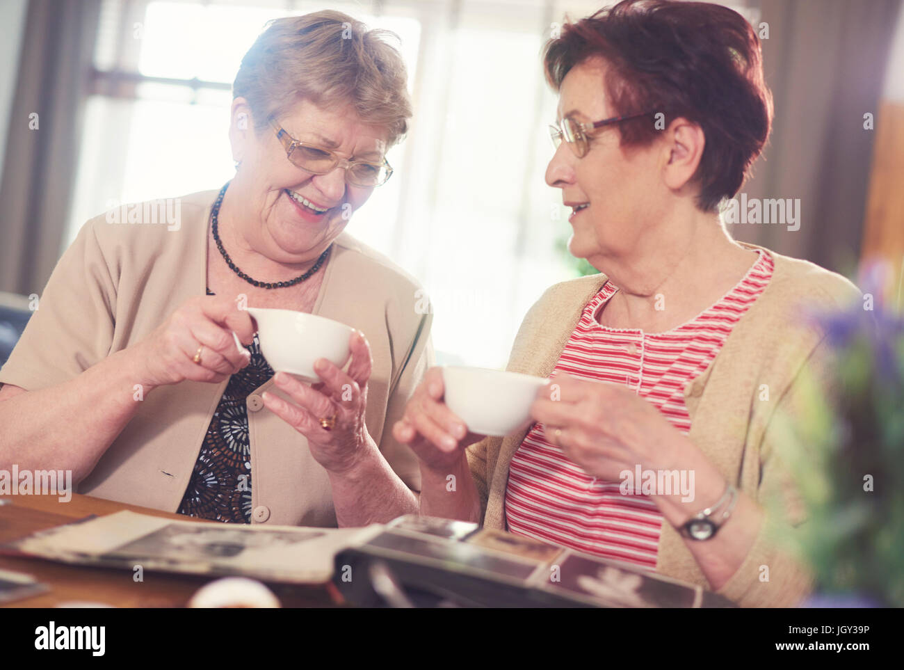 Two senior women laughing while looking at photo album on table Stock Photo