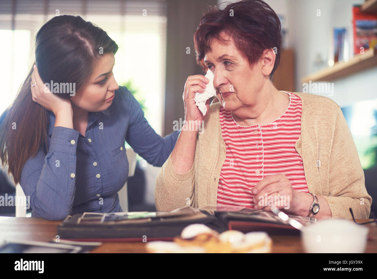 Young woman at table with grandmother crying while looking at photo album Stock Photo