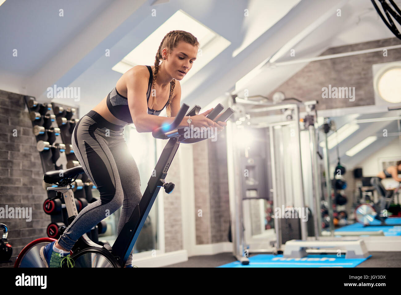 Young woman training, pedalling exercise bike in gym Stock Photo