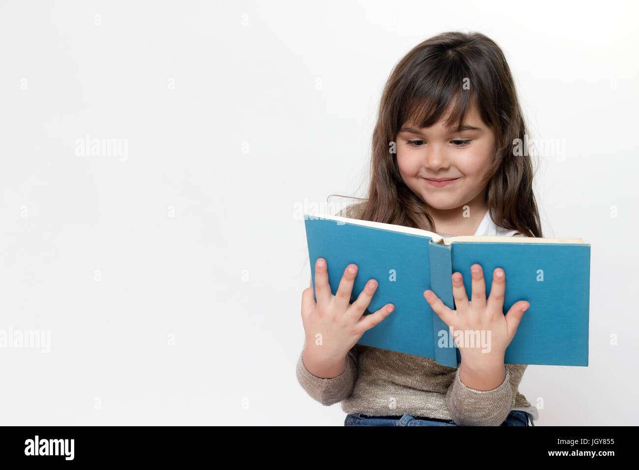 Front view of smiling long haired little girl holding and reading a book. All is on the light gray background. Stock Photo