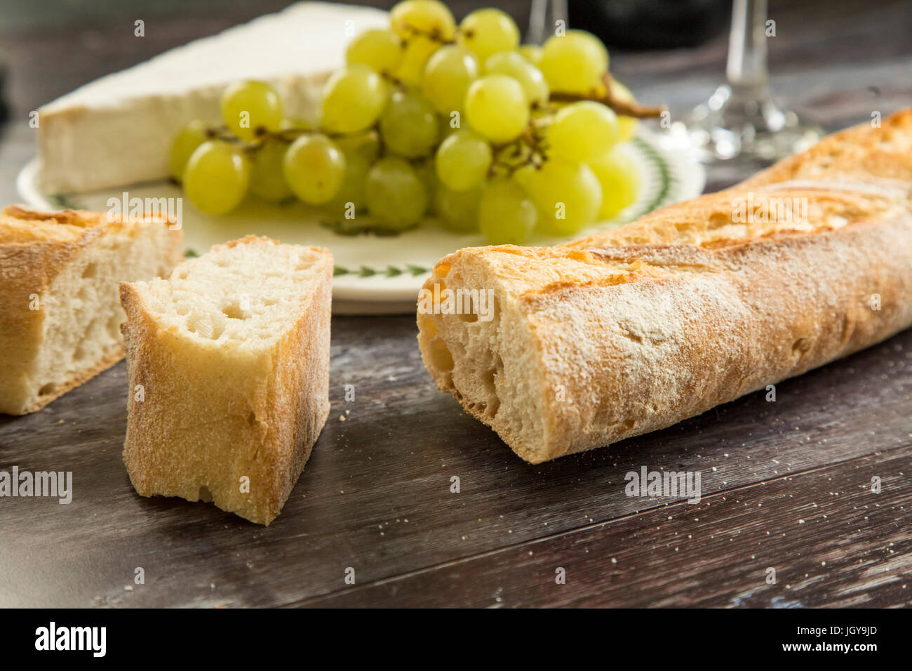 French bread, a wedge of brie cheese and grapes on a board. Stock Photo