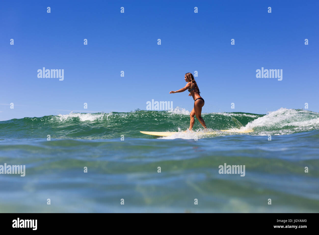 A healthy, tanned girl surfs over pristine clear water during summer in Australia. Stock Photo