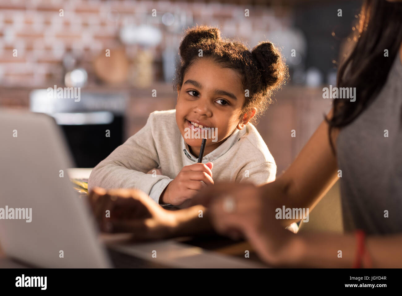 portrait of little girl doing homework with mother using laptop near by Stock Photo