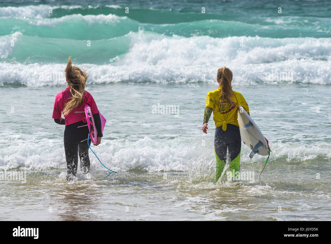 Surfing UK. Two young female surfers running into the sea as they compete in the UK Schools Surf Championship.; Nerf Clash of the Groms at Fistral in  Stock Photo