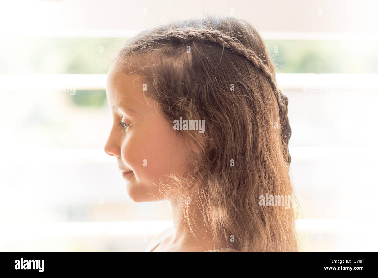 High-key portrait of girl with braided hair. Child with long brown with hairstyle with plaits, in front of window Stock Photo