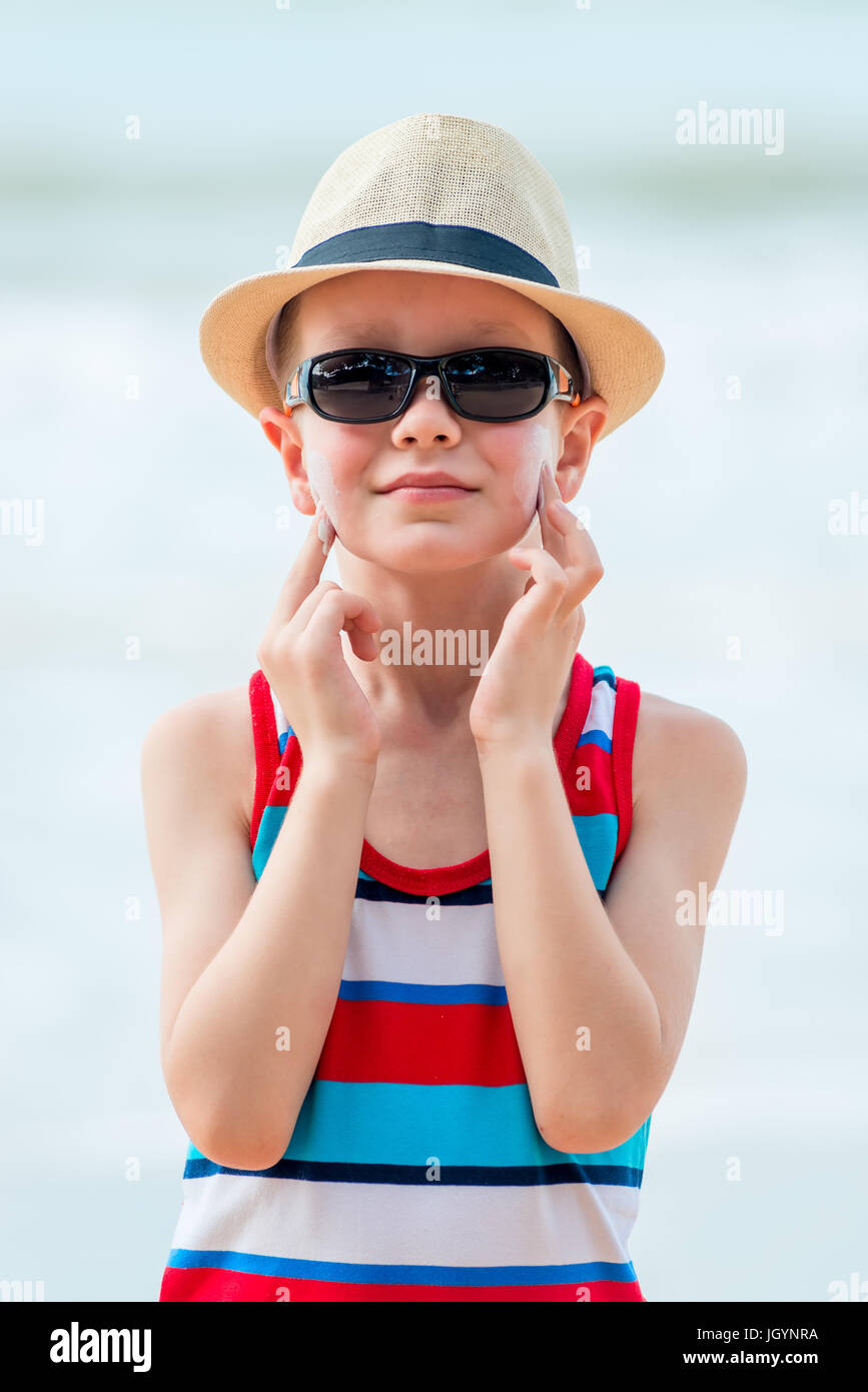 Boy on the beach wearing a hat and glasses smears his skin with sunscreen  Stock Photo - Alamy