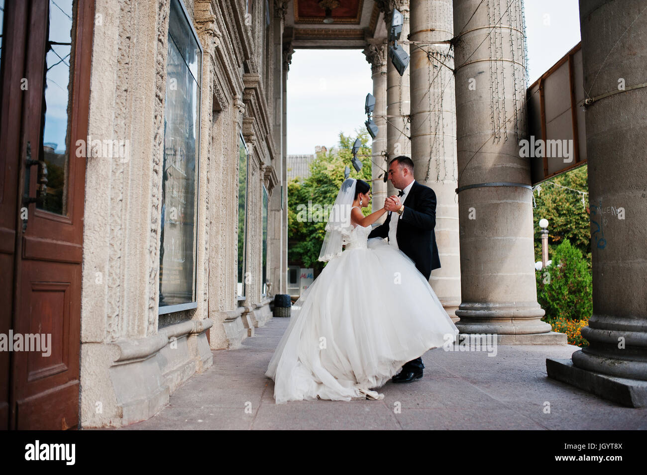 Fabulous wedding couple walking and posing next to the columns on a ...