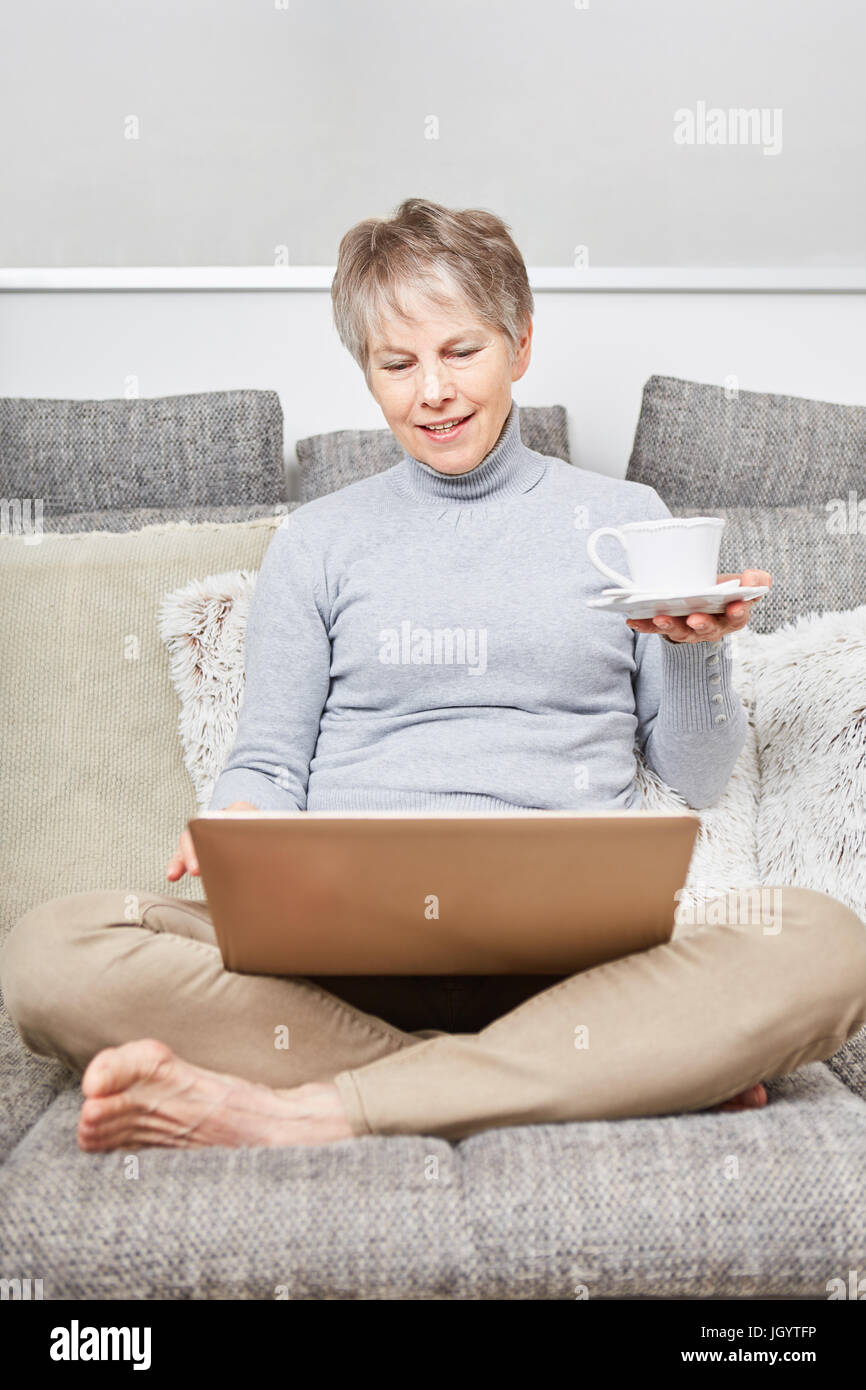 Senior woman uses laptop with relaxation while drinking cup of coffee Stock Photo