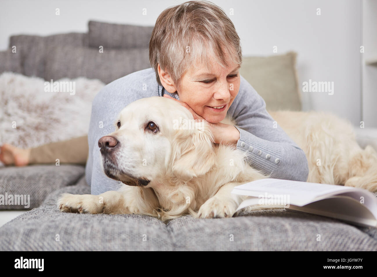Senior woman in relaxation with dog cuddles on the couch Stock Photo