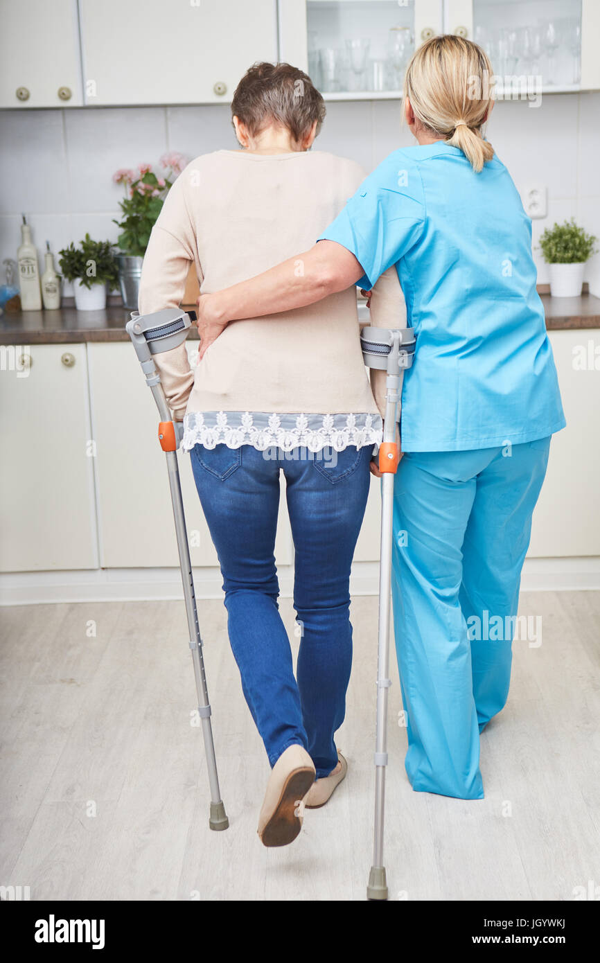 Senior woman with crutches in walk training with physiotherapy nurse