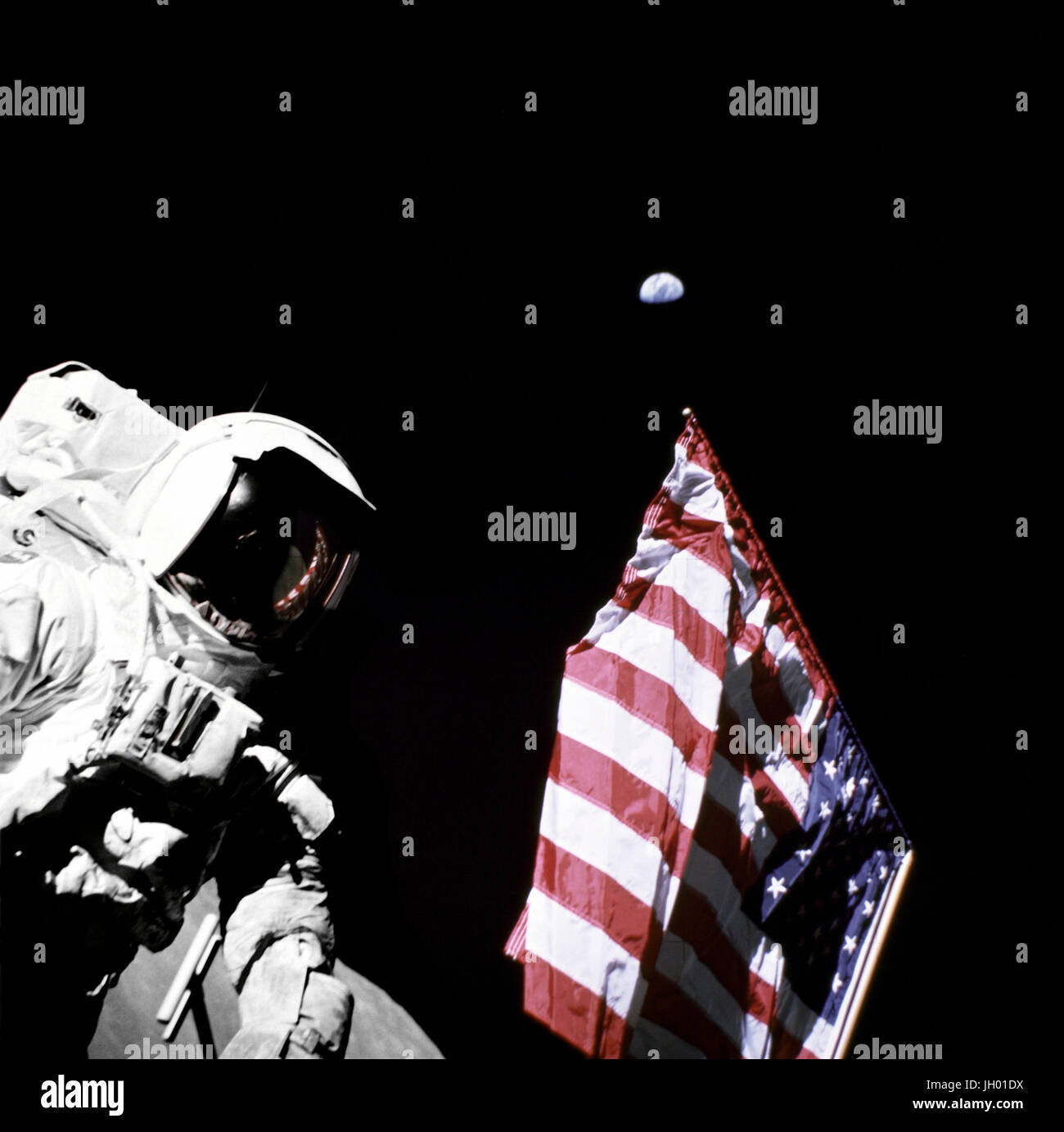Schmitt with Flag and Earth Above. Geologist-Astronaut Harrison Schmitt, Apollo 17 Lunar Module pilot, is photographed next to the American Flag during extravehicular activity (EVA) of NASA's final lunar landing mission in the Apollo series. The photo was taken at the Taurus-Littrow landing site. The highest part of the flag appears to point toward our planet earth in the distant background..Photographer: NASA Eugene Cernan Stock Photo