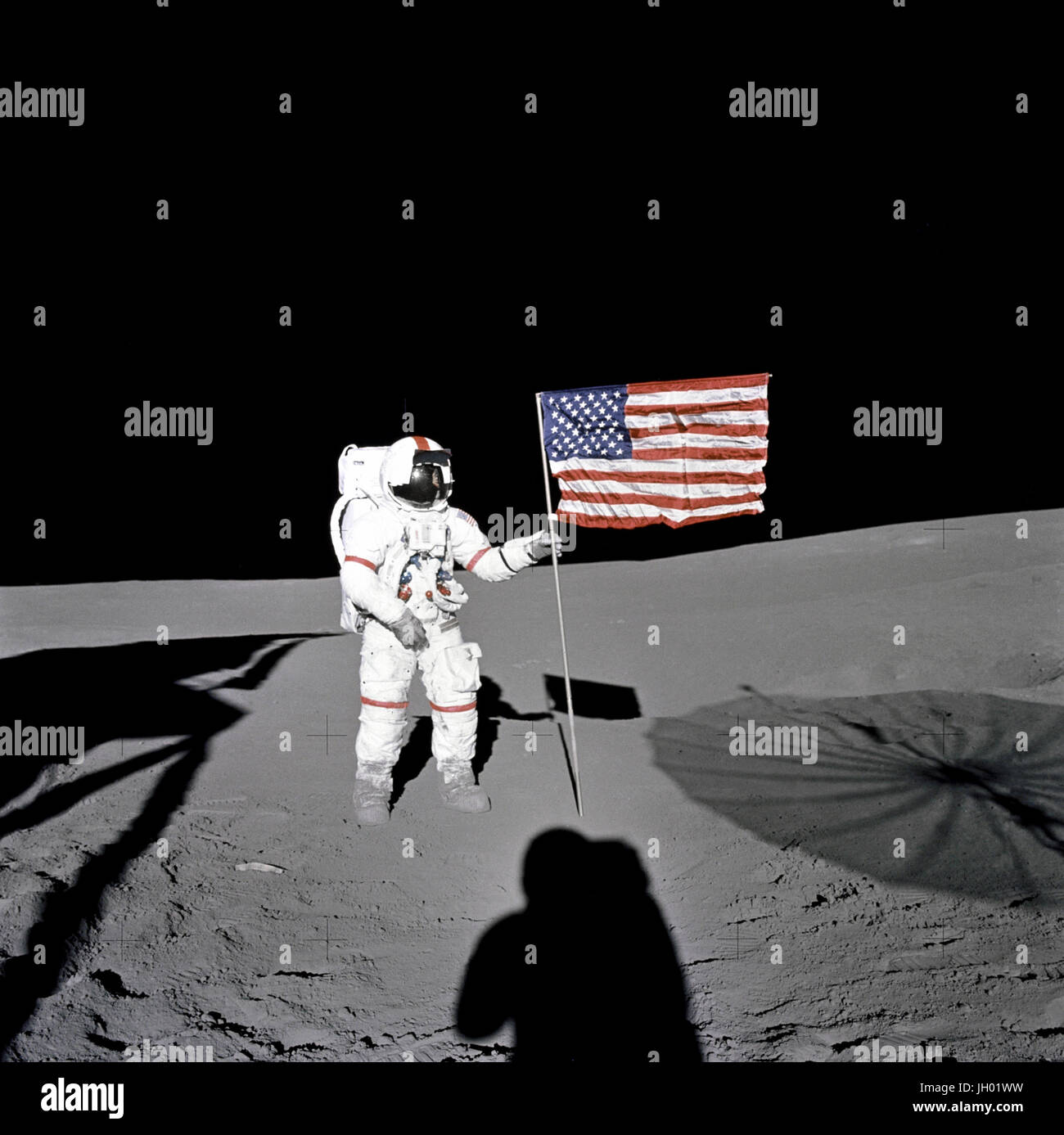 Astronaut Alan B. Shepard Jr., Apollo 14 Commander, stands by the U.S. flag on the lunar Fra Mauro Highlands during the early moments of the first extravehicular activity (EVA-1) of the mission. Shadows of the Lunar Module 'Antares', astronaut Edgar D. Mitchell, Lunar Module pilot, and the erectable S-band Antenna surround the scene of the third American flag planting to be performed on the lunar surface. NASA Photo Stock Photo