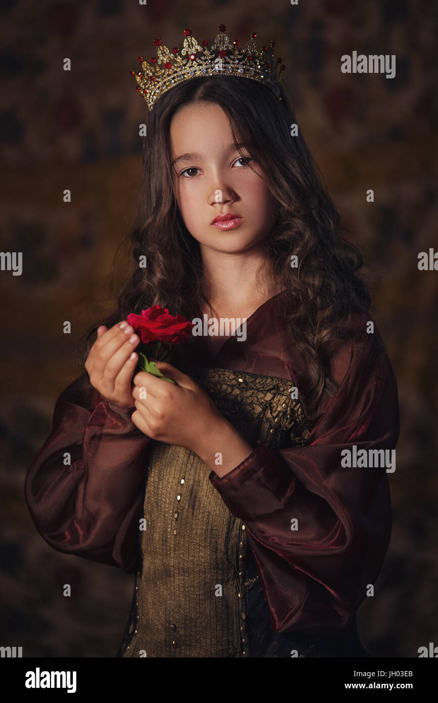 Portrait of cute girl wearing a crown with a rose in hands. Young queen or princess Stock Photo