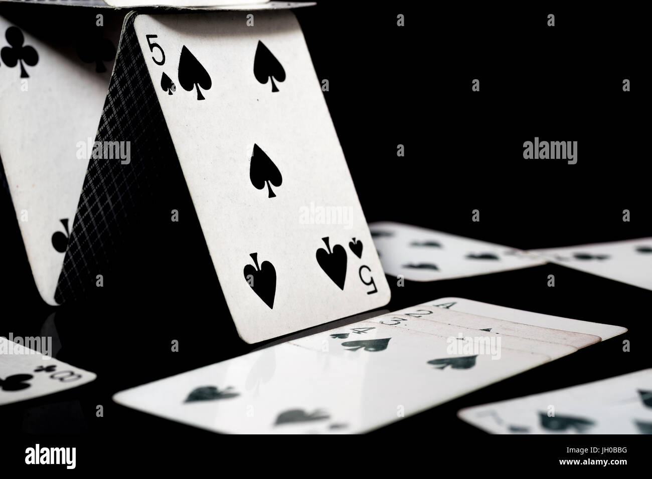 Playing cards forming a house of cards, and scattered white playing cards, black surface and background Stock Photo