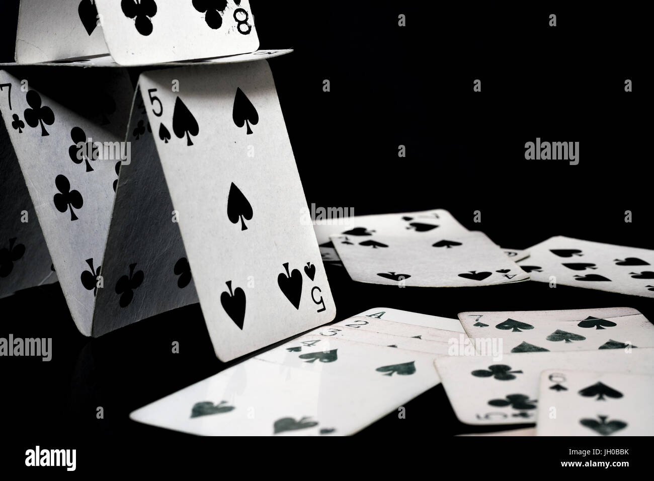 Playing cards forming a house of cards, and scattered white playing cards, black surface and background Stock Photo