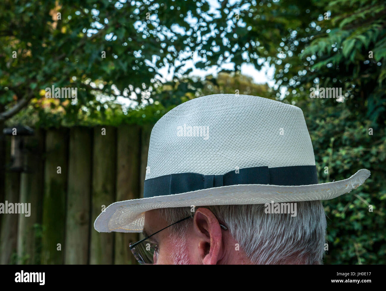 Close up of older man with white hair sitting outside ingarden wearing a Panama hat and face hidden, London, England, UK Stock Photo