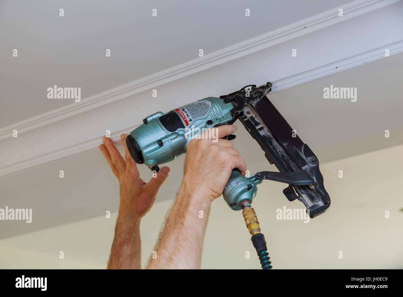 Carpenter brad using nail gun to Crown Moulding framing trim, with the