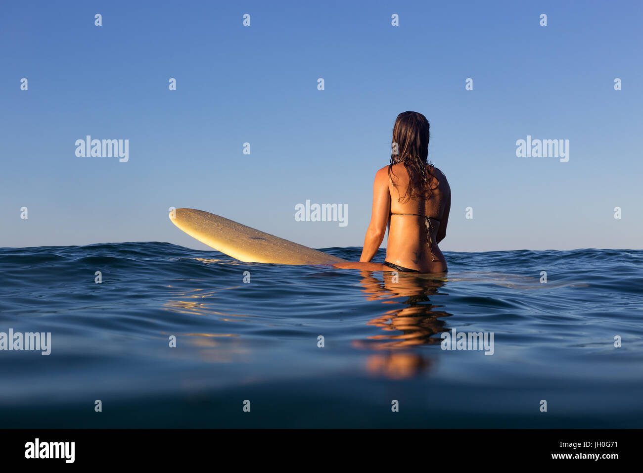 A surfer sits on her board and waits for a wave on a glassy calm ocean in Australia. Stock Photo