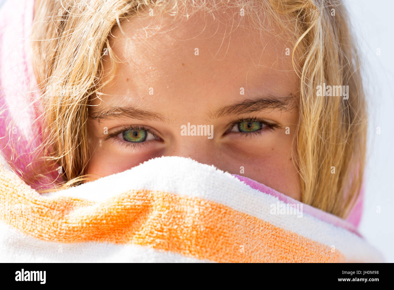 A vibrantly healthy young girl hides her cheeky smile behind a towel while on holidays at the beach. Stock Photo