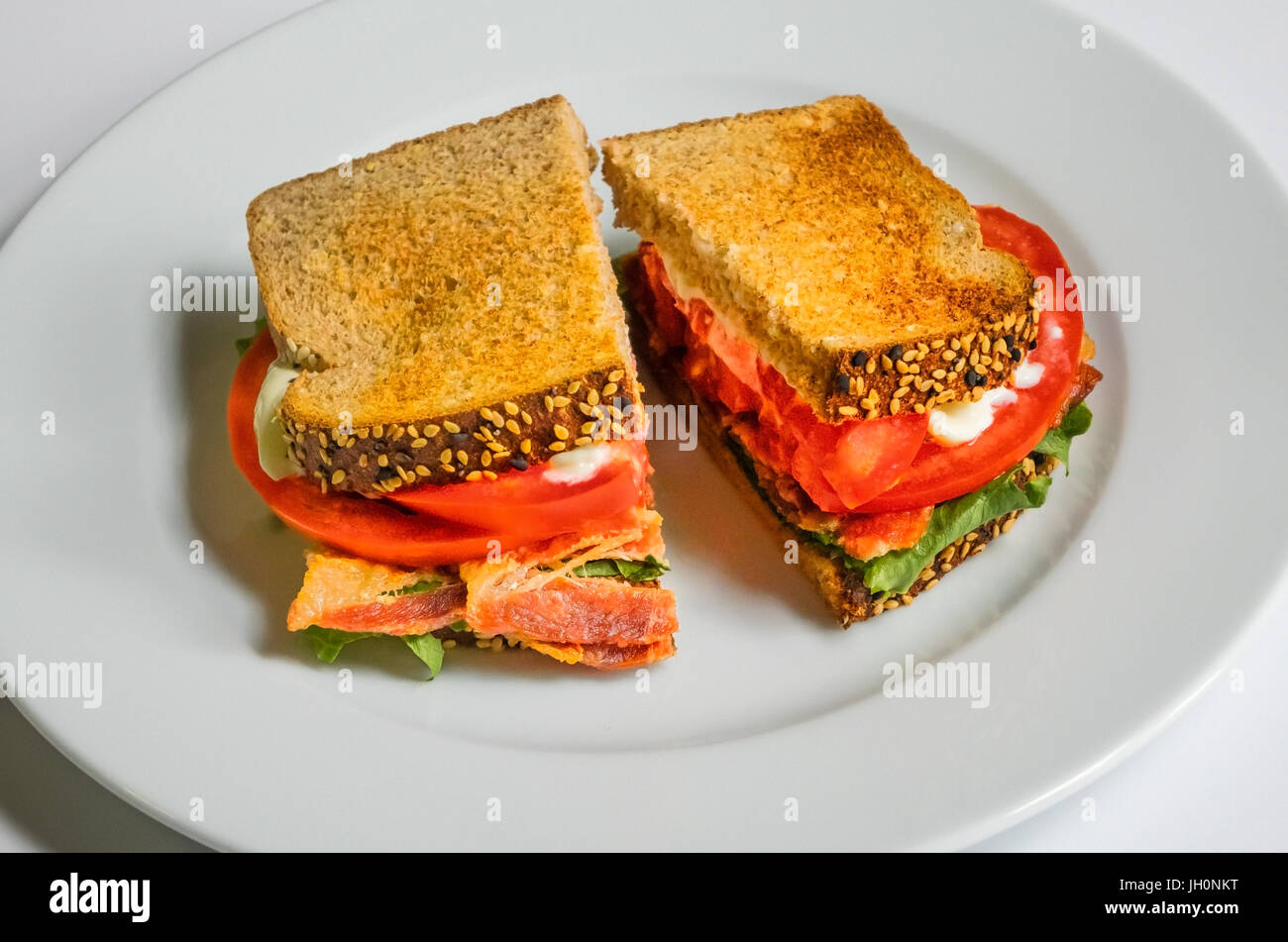 A BLT on a white dish, with bacon, lettuce, tomato, and mayonnaise on toasted wholewheat bread, a classic American sandwich Stock Photo
